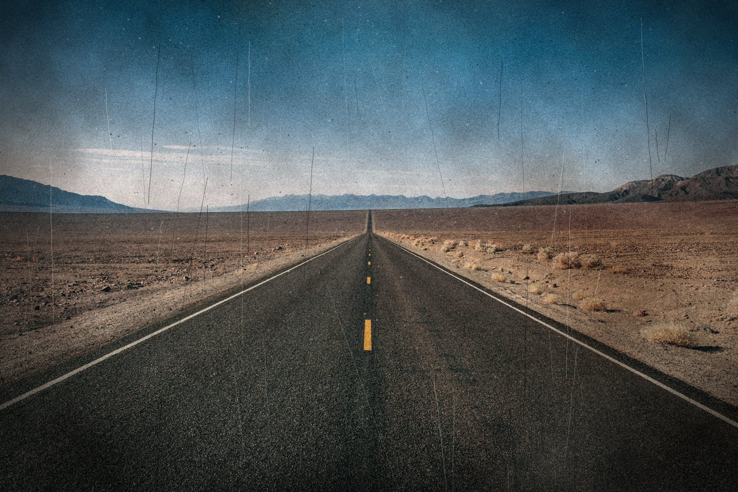 An empty two-lane desert road running straight to the mountains on the horizon